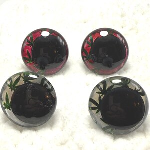 Peut inclure: Quatre cabochons ronds et transparents avec un centre sombre. Deux ont un motif de feuilles rouges et vertes sur le bord, et deux ont un motif de feuilles vertes. Les cabochons sont pos&eacute;s sur un fond blanc textur&eacute;.