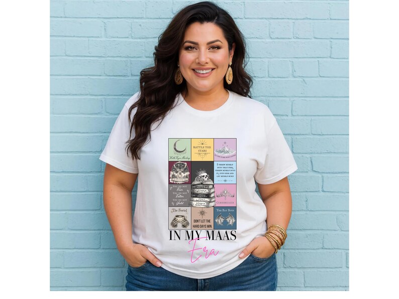 K&ouml;nnte beinhalten: Wei&szlig;es T-Shirt mit einem farbenfrohen Grafikdesign von Buchcovern und dem Text "IN MY MAAS Era" in rosa Schrift. Die Person tr&auml;gt das T-Shirt vor einer hellblauen Backsteinmauer.