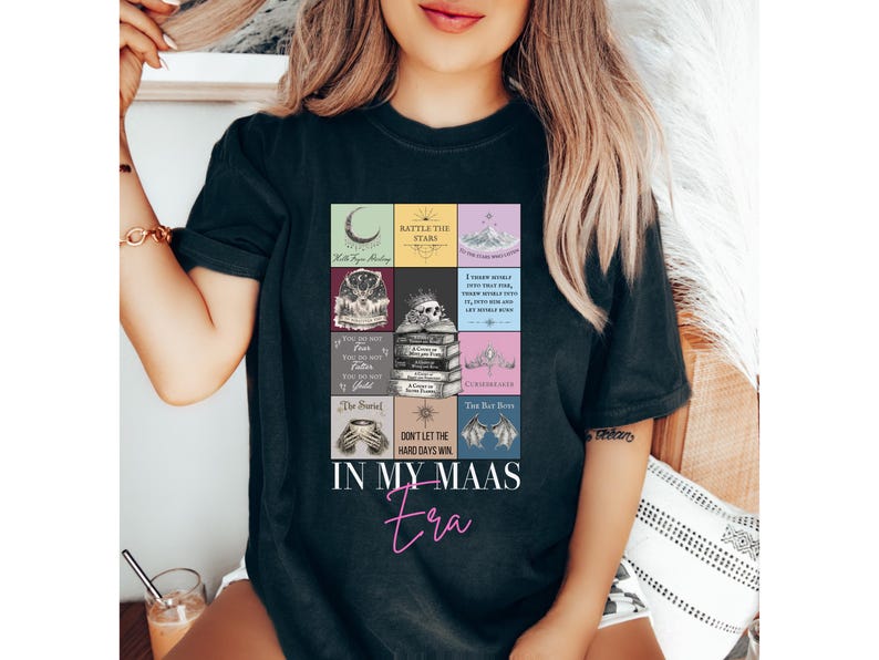 K&ouml;nnte beinhalten: Schwarzes T-Shirt mit einem farbenfrohen Grafikdesign mit Buchcovern und dem Text "IN MY MAAS Era". Das Design enth&auml;lt den Text "BATTLE THE STARS" und "DON'T LET THE HARD DAYS WIN".