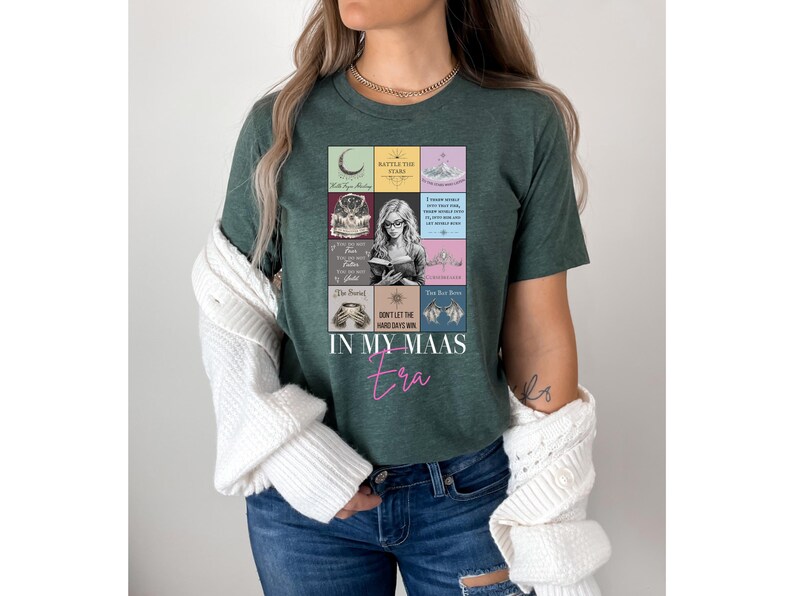 K&ouml;nnte beinhalten: Dunkelgr&uuml;nes T-Shirt mit einer farbenfrohen Grafik mit Buchmotiven und Text. Der Text "IN MY MAAS era" ist in rosa Schrift geschrieben. Das Shirt ist ein l&auml;ssiger Stil.