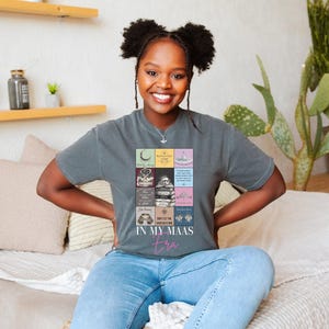 K&ouml;nnte beinhalten: Ein graues T-Shirt mit einem farbenfrohen Grafikdesign mit verschiedenen Bildern und dem Text "IN MY MAAS era" in Pink. Das T-Shirt wird von einer Person getragen.