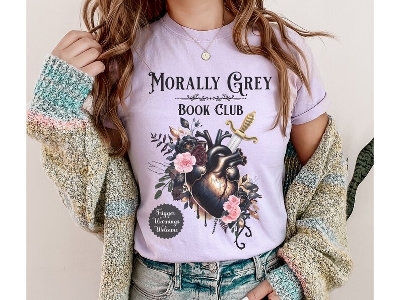 May include: A light purple t-shirt with the text "Morally Grey Book Club" above a graphic of a heart pierced by a sword, surrounded by flowers. The shirt also has a small graphic that says "Trigger Warnings Welcome".