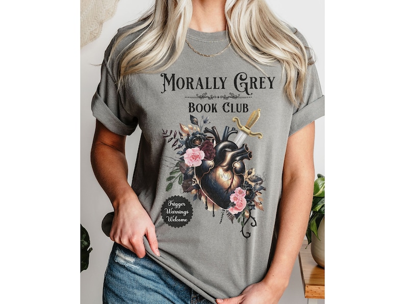 May include: Gray t-shirt with the text "Morally Grey Book Club" above a graphic of a heart pierced by a sword, surrounded by flowers. The shirt also has the text "Trigger Warnings Welcome".