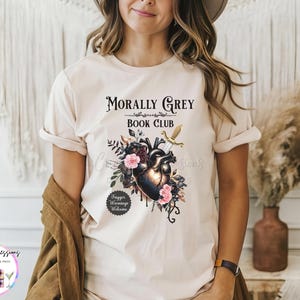 May include: Beige t-shirt with the text "Morally Grey Book Club" above a graphic of a heart, flowers, and a sword. The shirt also has the text "Trigger Warnings Welcome".