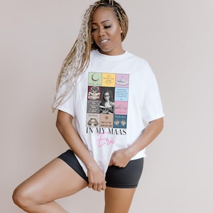 K&ouml;nnte beinhalten: Wei&szlig;es T-Shirt mit einer bunten Grafik mit Buchcovern und dem Text "IN MY MAAS era" in rosa Schrift. Das T-Shirt wird von einer Person getragen, die schwarze Shorts tr&auml;gt.