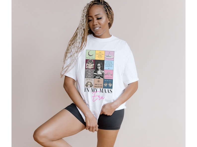 K&ouml;nnte beinhalten: Wei&szlig;es T-Shirt mit einer bunten Grafik mit Buchcovern und dem Text "IN MY MAAS era" in rosa Schrift. Das T-Shirt wird von einer Person getragen, die schwarze Shorts tr&auml;gt.