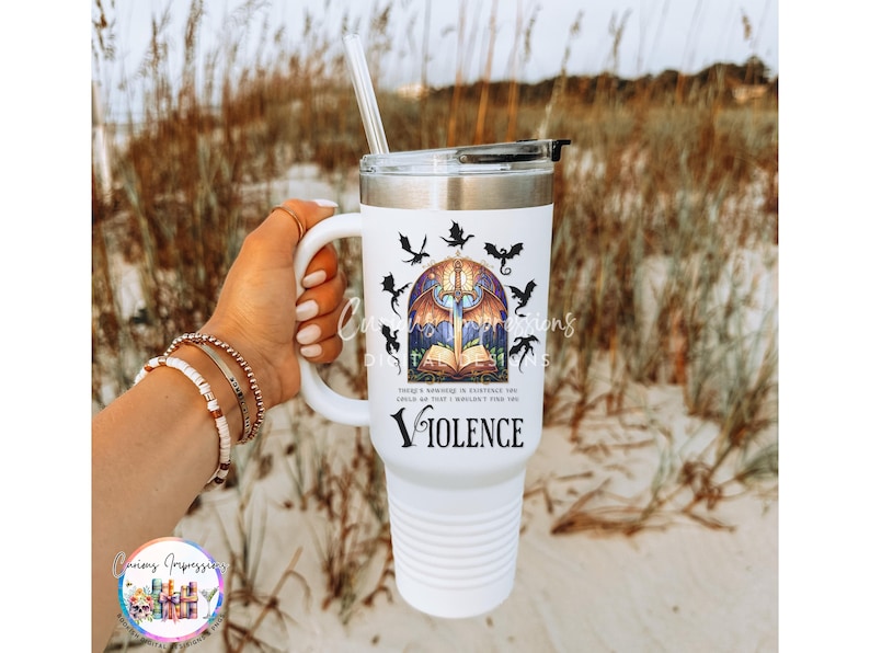 May include: White travel mug with a handle, featuring a design with a sword, open book, and bats. The word "Violence" is printed below the design. Includes a straw and a black lid.