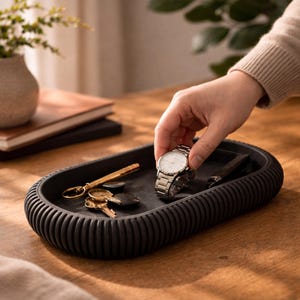 Hand legt Uhr in schwarze Japandi Ablageschale auf Holztisch – stilvolle Schlüssel- und Schmuckablage im minimalistischen Design.