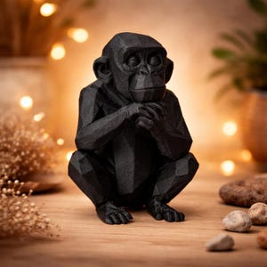 Könnte beinhalten: Eine schwarze Schimpansenfigur in sitzender Position, die Hände am Kinn verschränkt. Die Skulptur hat ein geometrisches, facettiertes Design und steht auf einer Holzoberfläche. Der Hintergrund zeigt weiche Beleuchtung und dekorative Elemente.