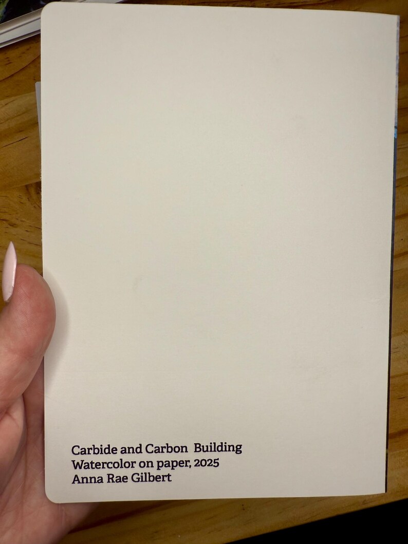 Puede incluir: Un papel rectangular blanquecino con el texto "Carbide and Carbon Building, Watercolor on paper, 2025, Anna Rae Gilbert" impreso en negro. El papel est&aacute; sostenido por una persona.