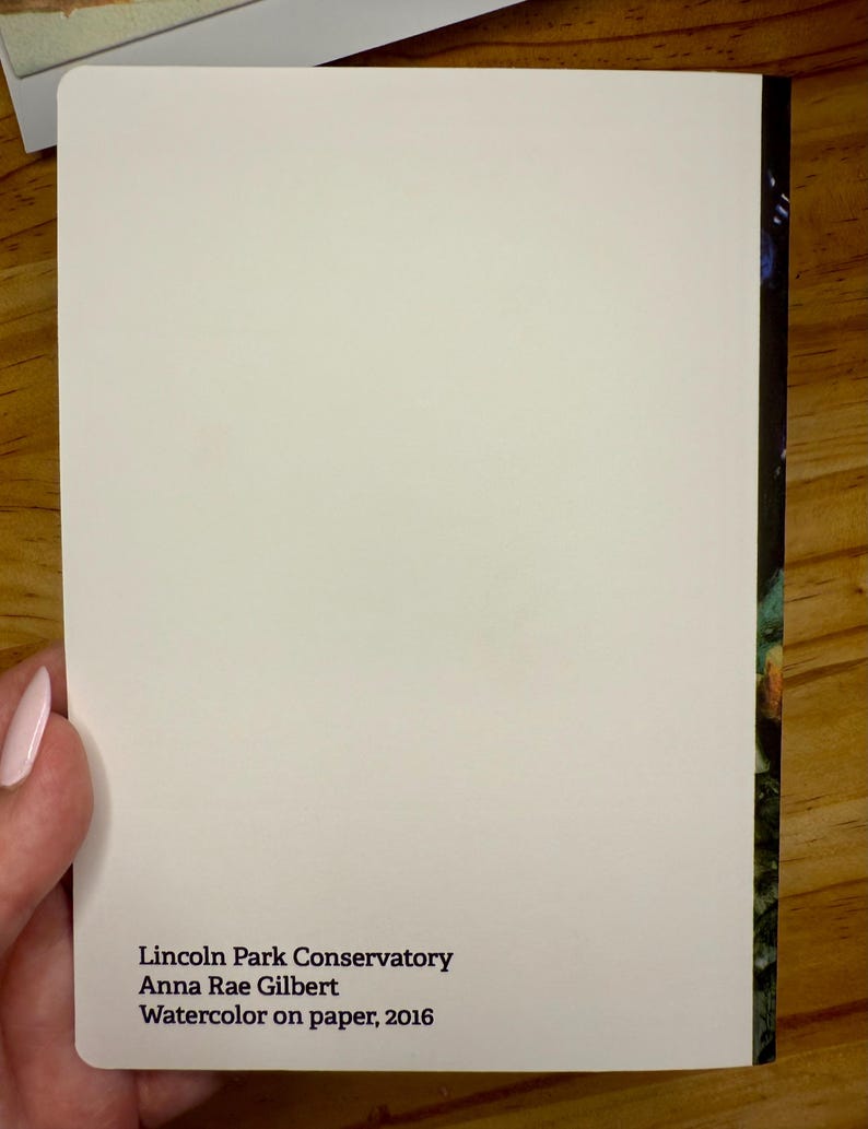 Puede incluir: Una tarjeta rectangular blanca con esquinas redondeadas, sostenida por una mano. La tarjeta presenta el texto: "Lincoln Park Conservatory, Anna Rae Gilbert, Watercolor on paper, 2016." El borde derecho muestra un vistazo de una imagen colorida.