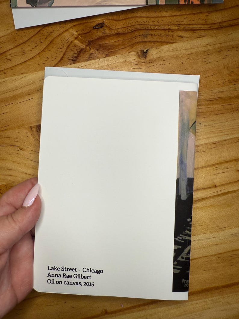 Puede incluir: Una tarjeta de felicitaci&oacute;n blanca con el texto "Lake Street - Chicago Anna Rae Gilbert Oil on canvas, 2015" se sostiene contra una superficie de madera. La tarjeta tiene una peque&ntilde;a secci&oacute;n de una pintura en el lado derecho.