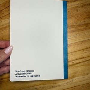 Puede incluir: Una pintura de acuarela blanca titulada "Blue Line - Chicago" de Anna Rae Gilbert, 2015. La pintura tiene un lomo azul y est&aacute; sobre papel. La pintura est&aacute; sostenida por una persona.