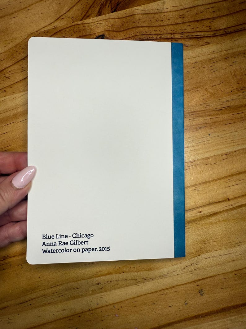 Puede incluir: Una pintura de acuarela blanca titulada "Blue Line - Chicago" de Anna Rae Gilbert, 2015. La pintura tiene un lomo azul y est&aacute; sobre papel. La pintura est&aacute; sostenida por una persona.