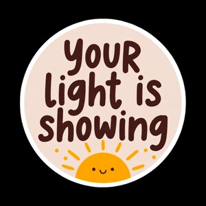 May include: A round sticker with the text "YOUR light is showing" in brown letters. The sticker has a light peach background and a smiling yellow sun graphic at the bottom. The sticker is outlined in white.