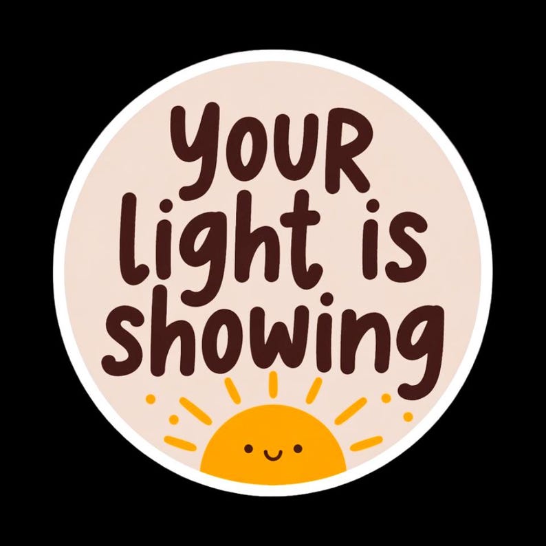 May include: A round sticker with the text "YOUR light is showing" in brown letters. The sticker has a light peach background and a smiling yellow sun graphic at the bottom. The sticker is outlined in white.