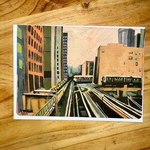 Puede incluir: Una pintura a la acuarela de un paisaje urbano con v&iacute;as de tren elevadas, edificios y un tren. La obra de arte est&aacute; firmada "Anne Rae 2017" en la esquina inferior izquierda. Los edificios est&aacute;n pintados en tonos naranja, verde y gris.