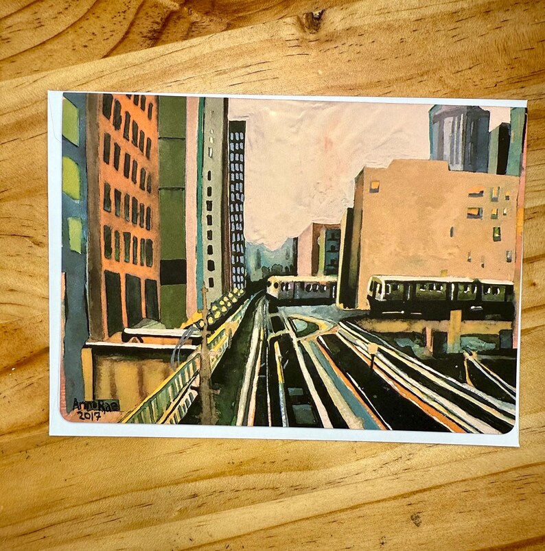 Puede incluir: Una pintura a la acuarela de un paisaje urbano con v&iacute;as de tren elevadas, edificios y un tren. La obra de arte est&aacute; firmada "Anne Rae 2017" en la esquina inferior izquierda. Los edificios est&aacute;n pintados en tonos naranja, verde y gris.