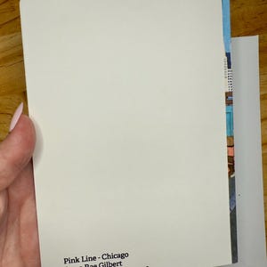 Puede incluir: Una tarjeta rectangular blanca con esquinas redondeadas, sostenida en una mano, con el texto "Pink Line - Chicago Anna Rae Gilbert Watercolor on paper, 2018." Una colorida pintura de acuarela es visible en el borde de la tarjeta.