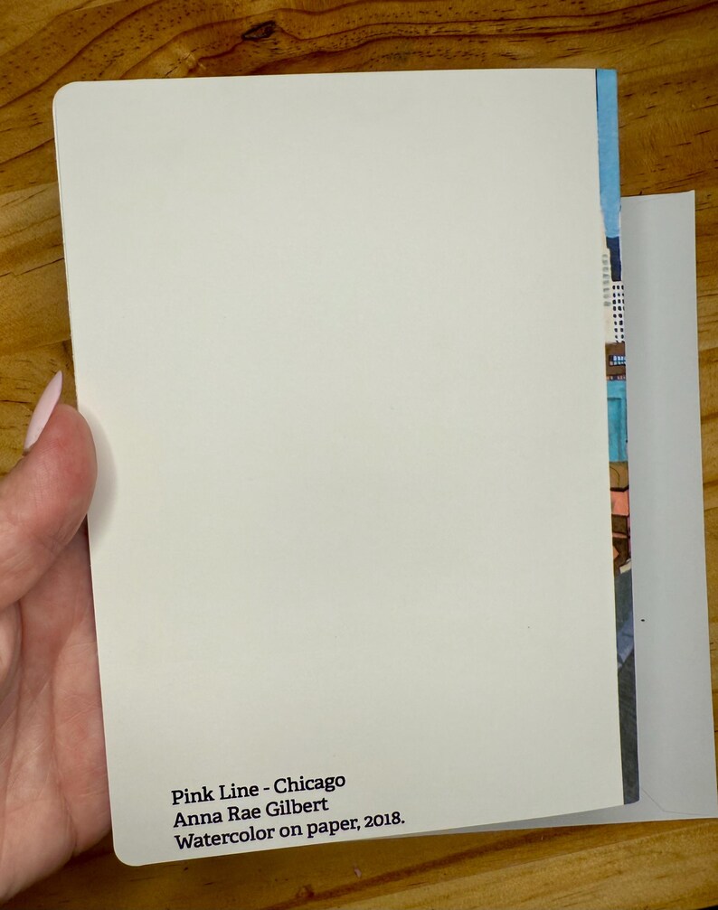Puede incluir: Una tarjeta rectangular blanca con esquinas redondeadas, sostenida en una mano, con el texto "Pink Line - Chicago Anna Rae Gilbert Watercolor on paper, 2018." Una colorida pintura de acuarela es visible en el borde de la tarjeta.