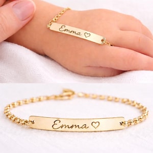Könnte beinhalten: Ein goldfarbenes Kettenarmband mit einer flachen, rechteckigen Identifikationsplatte, die mit dem Namen Emma und einem kleinen Herzsymbol graviert ist. Das Armband hat ein feines Gliederkettendesign und eine polierte Oberfläche.