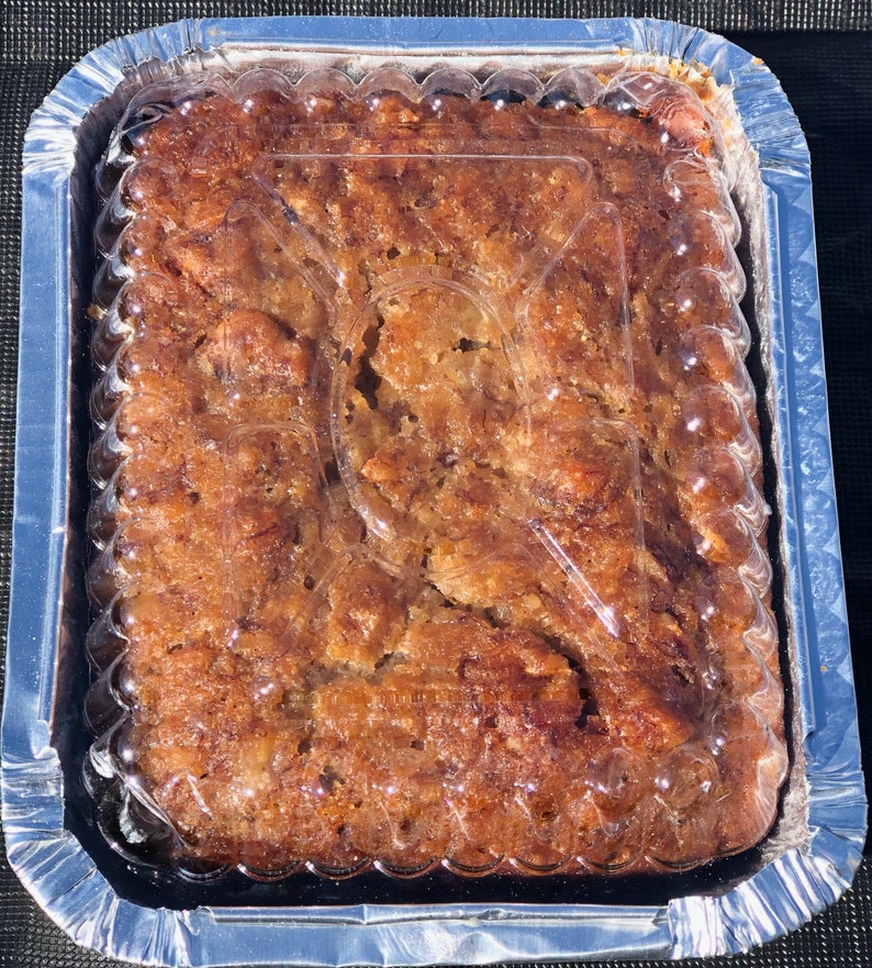 May include: A close-up of a rectangular pan of banana bread with a clear plastic lid. The bread is a light brown color and has a slightly crispy top.