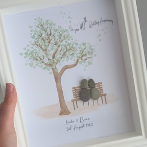 May include: A framed artwork featuring a tree with green heart-shaped leaves, a couple sitting on a bench, and the text "On your 40th Wedding Anniversary Linda & Brian 3rd August 1983".