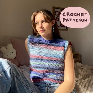 Puede incluir: Un top de ganchillo a rayas en azul, rosa y verde. El top tiene cuello redondo y sin mangas. El texto "CROCHET PATTERN" está en una burbuja rosa.