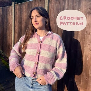 Könnte beinhalten: Ein Häkelmuster für eine gestreifte Strickjacke mit rosa und weißen Streifen. Die Strickjacke hat einen Knopfverschluss und lange Ärmel.