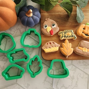 May include: A set of green plastic cookie cutters in various shapes, including a pumpkin, a turkey, a leaf, a pie, a hat, and a banner that says "Give Thanks".