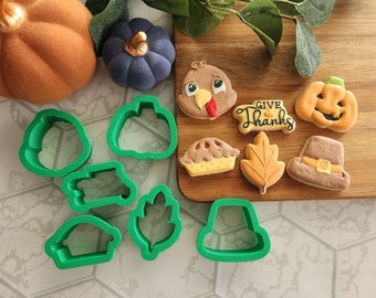 May include: A set of green plastic cookie cutters in various shapes, including a pumpkin, a turkey, a leaf, a pie, a hat, and a banner that says "Give Thanks".