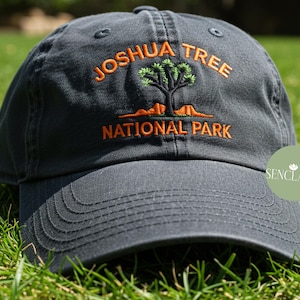 May include: A dark blue baseball cap with an embroidered design of a Joshua Tree National Park logo in orange and green.