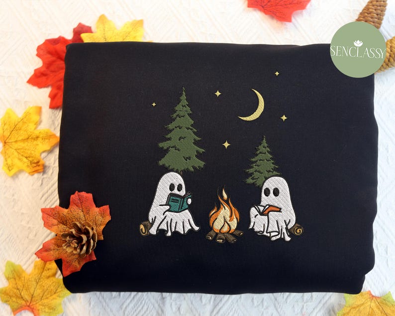 May include: Black sweatshirt with an embroidered design of two ghosts reading books by a campfire in a forest. The design includes a crescent moon and stars.