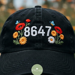 May include: Black baseball cap with embroidered red and yellow flowers, butterflies, and the number 8647.