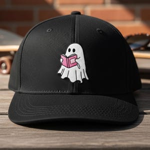 May include: Black baseball cap with a curved brim. The cap features a white ghost patch reading a pink book. The ghost has a friendly expression. The cap is made of a durable fabric and has a structured fit.