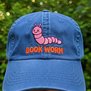 May include: A blue baseball cap with an embroidered pink worm and the text "BOOK WORM" in orange.