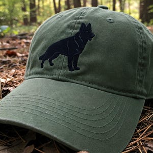 May include: A green baseball cap with a black silhouette of a German Shepherd dog embroidered on the front.