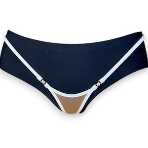 Puede incluir: Ropa interior negra con ribete y tirantes blancos. El panel frontal es de color marr&oacute;n claro. Las correas est&aacute;n conectadas con peque&ntilde;os detalles dorados.