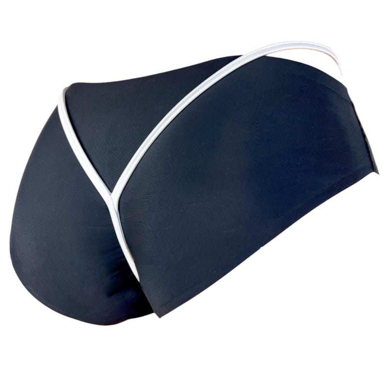 Puede incluir: Ropa interior negra con ribete blanco. La prenda tiene una cintura baja y una espalda tipo tanga. El ribete blanco perfila los bordes de la ropa interior, creando un dise&ntilde;o contrastante. La tela parece suave y ajustada.