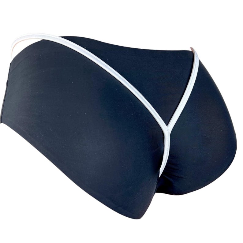 Puede incluir: Braguita de traje de ba&ntilde;o negra con ribete blanco. La braguita tiene cintura baja y corte cheeky. El ribete blanco perfila los bordes y crea un dise&ntilde;o contrastante. La tela parece suave y ajustada.