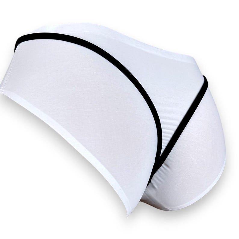 Puede incluir: Ropa interior blanca con ribete negro. La ropa interior presenta un dise&ntilde;o minimalista con una apariencia suave y sin costuras. El ribete negro perfila los bordes y agrega un detalle de contraste a la tela blanca. El estilo general es simple y moderno.