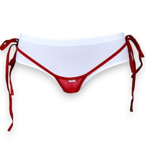 Könnte beinhalten: Weiße Unterwäsche mit rotem Besatz und Bändern. Die Unterwäsche hat ein rotes Netzpanel vorne.
