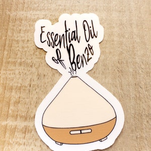 May include: A white sticker with a black outline of an essential oil diffuser and the text "Essential Oil of Benzo" in black cursive.