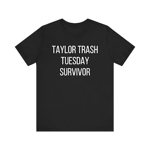 May include: Black t-shirt with the white text "TAYLOR TRASH TUESDAY SURVIVOR". The short-sleeved shirt is made of a soft material and has a crew neck. The text is centered on the front of the shirt.