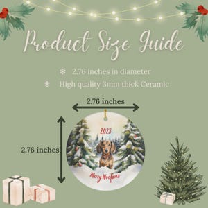 K&ouml;nnte beinhalten: Runder Weihnachtsbaumschmuck aus Keramik, 7 cm Durchmesser, mit einem Dackel in einer Winterszene mit dem Text "2023" und "Merry Woofmas". Der Anh&auml;nger ist 3 mm dick.