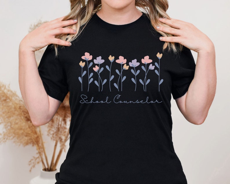 Puede incluir: Camiseta negra con un dise&ntilde;o floral y el texto "School Counselor" en blanco.