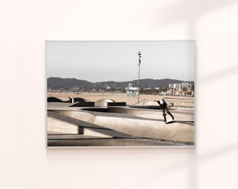 Peut inclure: Un skateboarder effectue un tour dans un skatepark en béton avec vue sur la plage et les montagnes en arrière-plan.