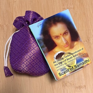 Könnte beinhalten: Ein violetter Kordelzugbeutel mit einem goldenen Diamantmuster neben einer Produktbox. Die Box zeigt ein Frauenporträt und den Text "All natural, herbal deodorant of the yogis of South India. Scent of Samadhi."