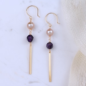 May include: Gold dangle earrings with a purple gemstone and a cream-colored pearl on each earring.