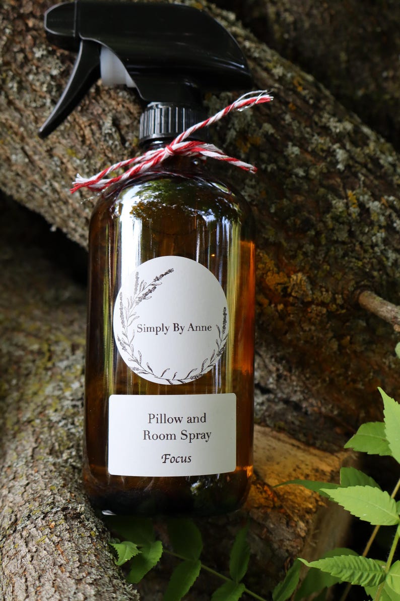 Pode incluir: Uma garrafa de vidro marrom com um bico de pulveriza&ccedil;&atilde;o preto e um r&oacute;tulo branco. O r&oacute;tulo diz "Simply By Anne" em um c&iacute;rculo com um design floral e "Pillow and Room Spray Focus".